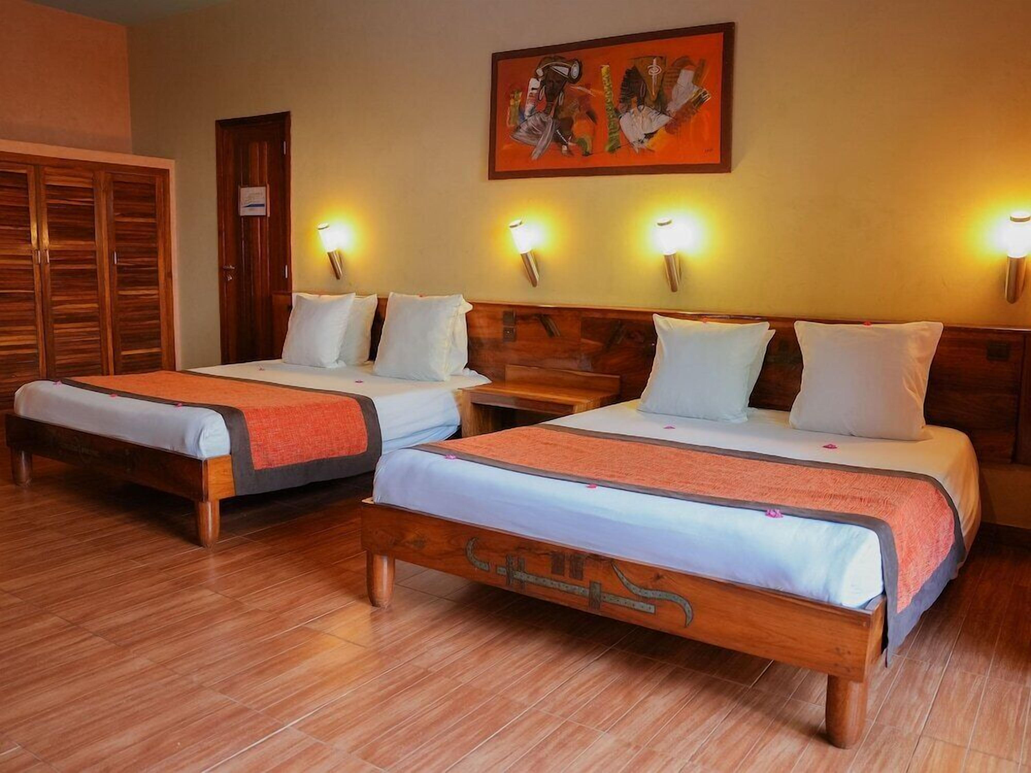 A hotel room with two wooden beds, a wooden wardrobe, and a painting on the wall.
