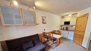 A compact living space with a sofa, dining table, chairs, a kitchenette, and a wooden door. - Cozy Studio with Cabin for 4/5 People, Near Ski Lifts - Modane, France (Valfréjus)