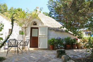 Una casa de piedra rústica con techo de paja, una puerta de madera y un pequeño porche con mobiliario exterior.