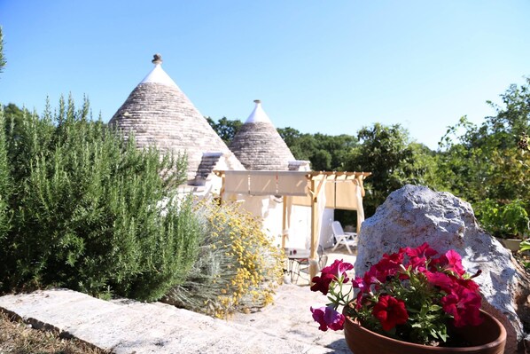 Una casa de piedra tradicional con techos cónicos, rodeada de follaje y una gran roca.