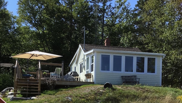 A small white cabin with a porch, surrounded by a gravel path and large rocks. - Ocean front cottage in the heart of Hubbards. (Hubbards)