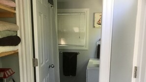A narrow hallway with a door on the left, a window with blinds, a small white appliance, and a red chair. - Ocean front cottage in the heart of Hubbards. (Hubbards)