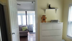 A bedroom with a bed, a dresser, and a door leading to a living area with a sofa and a window. - Ocean front cottage in the heart of Hubbards. (Hubbards)
