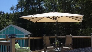 A wooden deck with outdoor furniture, including chairs and a table, under a large umbrella. - Ocean front cottage in the heart of Hubbards. (Hubbards)