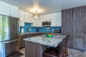 A kitchen with a marble island, stainless steel appliances, and a blue backsplash. - Beachfront Kihei condo with pool, hot tub and lanai summer deals (Kihei)