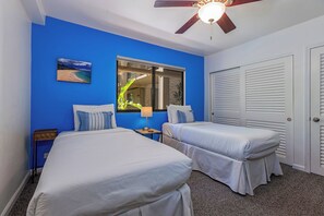 A room with two beds, a ceiling fan, a window with a view, and a door with louvered shutters. - Beachfront Kihei condo with pool, hot tub and lanai summer deals (Kihei)