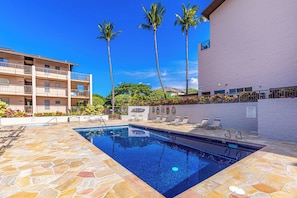 A swimming pool area with lounge chairs, a poolside bar, and palm trees. - Beachfront Kihei condo with pool, hot tub and lanai summer deals (Kihei)