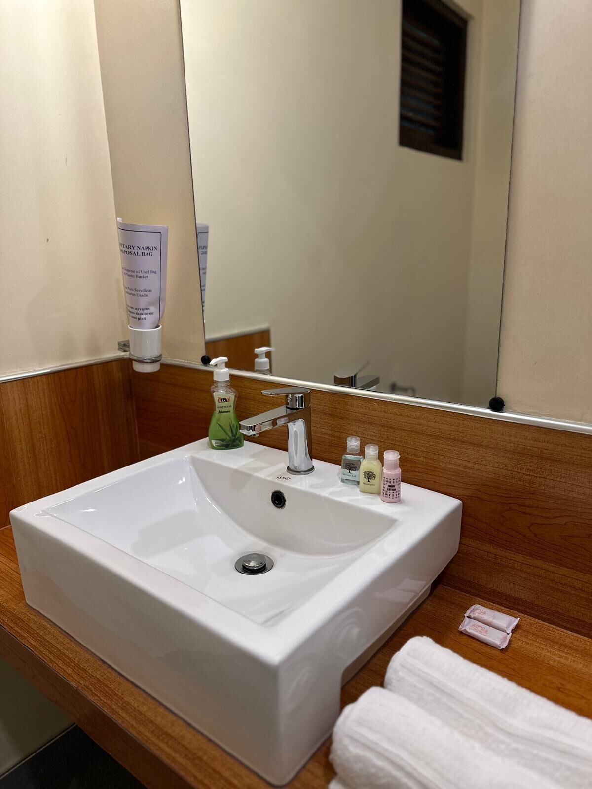 A hotel bathroom with a white sink, a mirror, and toiletries on the countertop.