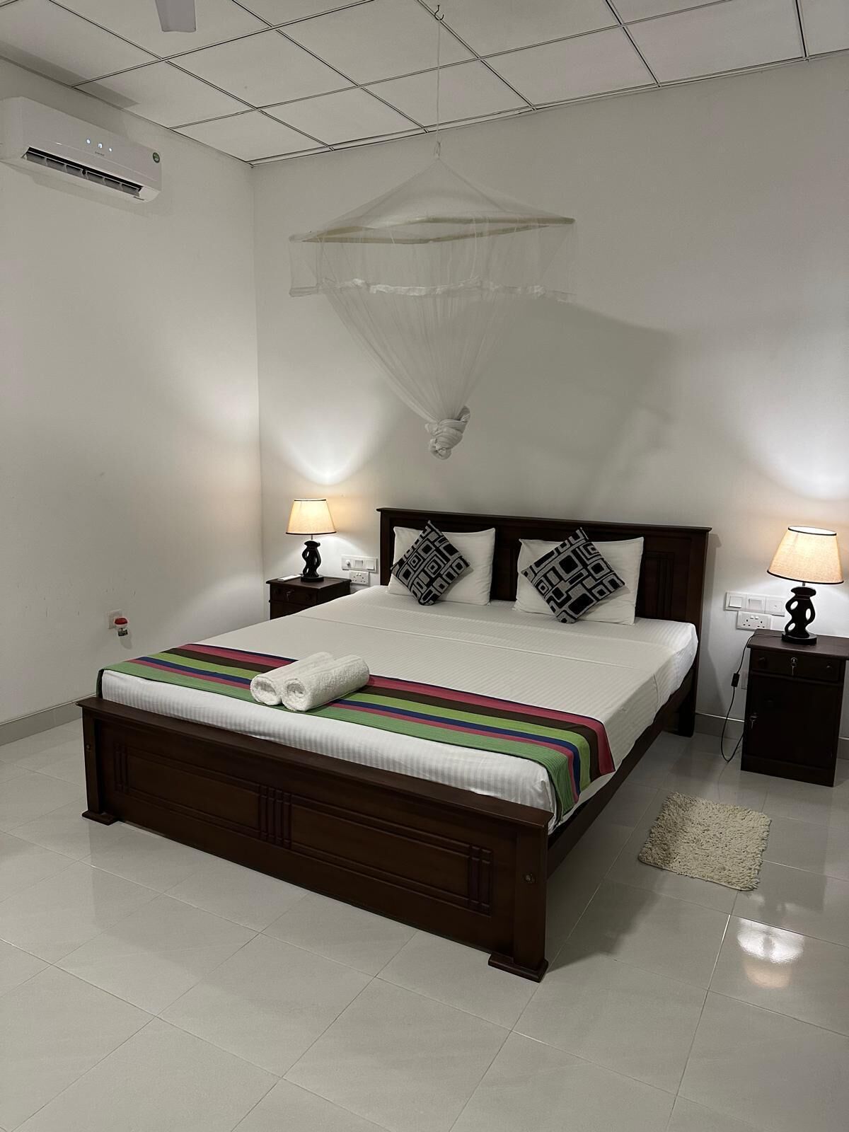 Un dormitorio con cama, mesitas de noche, mosquitero colgante y aire acondicionado instalado en la pared.