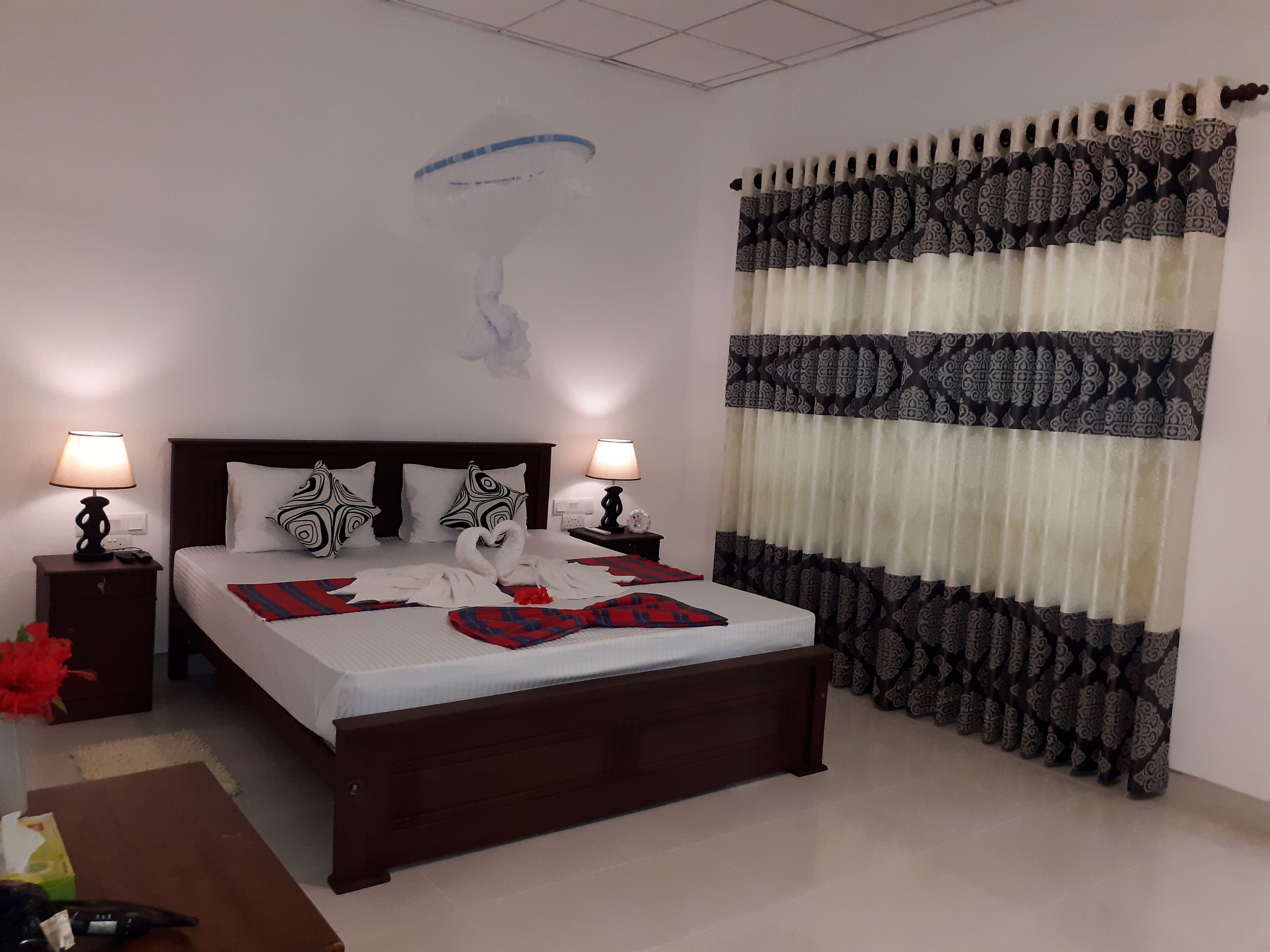 A neatly made bed with decorative pillows, a bedside table with a lamp, and a patterned curtain.