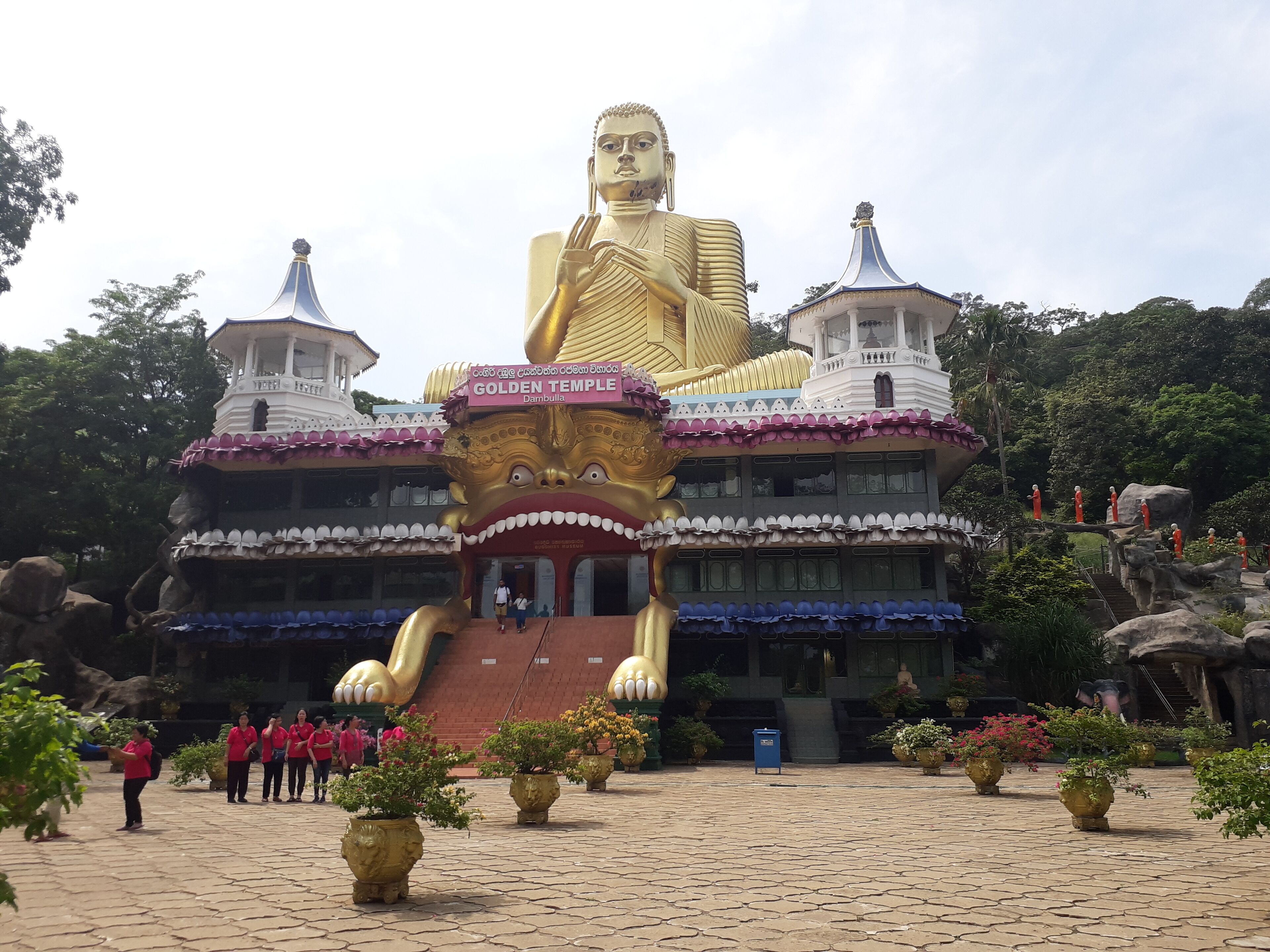Un'imponente statua dorata di Buddha di fronte a un tempio, con un cartello che riporta la scritta 'GOLDEN TEMPLE'.