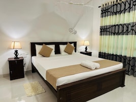 Habitación de hotel con una cama grande, dos mesitas de noche con lámparas y una mesita de noche con un objeto decorativo, además de una ventana con cortinas estampadas.