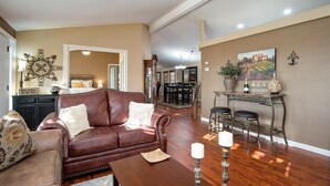 Ein Wohnzimmer mit braunem Ledersofa, einem Essbereich mit einer Chandelieber und einer Wand mit einem Gemälde von Weinbergen.
