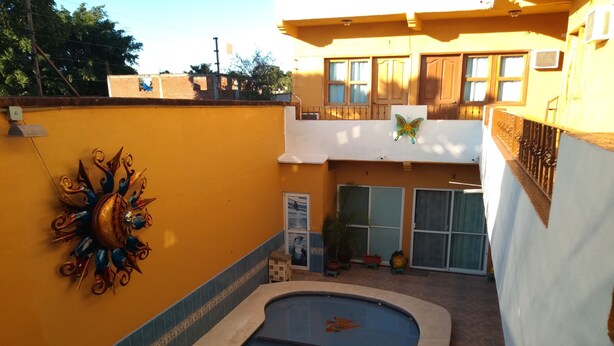 A swimming pool area with a decorative sun sculpture, a small seating area, and a view of a building with a balcony. - A peaceful apartment in sun house Puerto Vallarta (Lomas del Calvario)