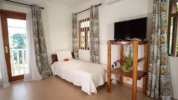 A bedroom with a bed, a TV on a wooden stand, and a balcony with curtains.