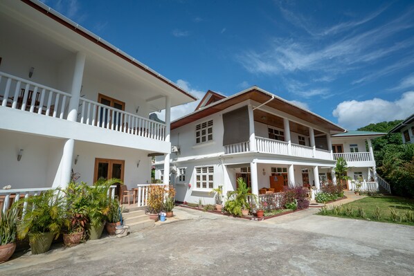 A two-story white building with balconies, potted plants, and a clear blue sky. - La Maison Hibiscus (Mahé Island)