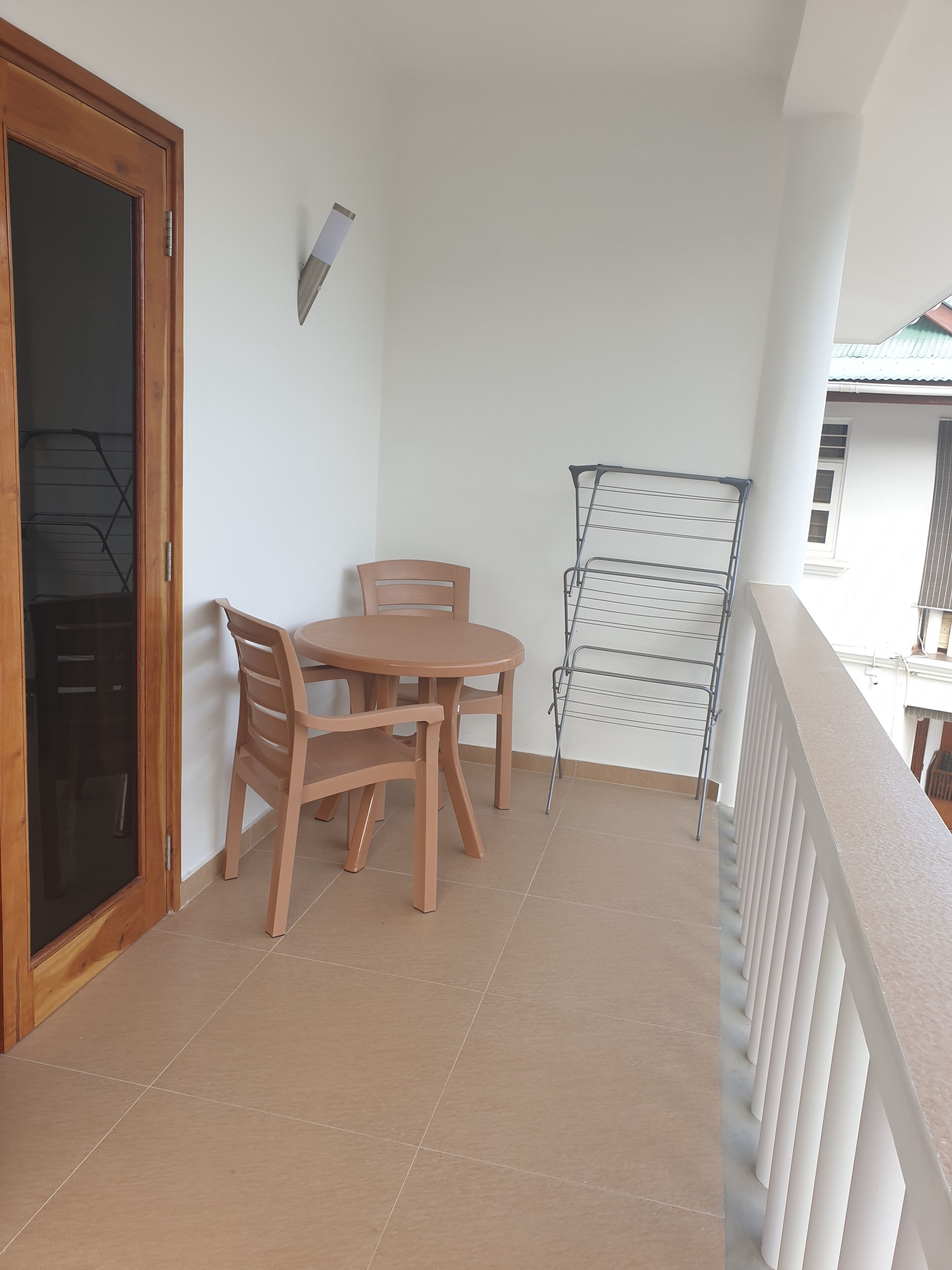 A balcony with a wooden table and chairs, a clothes drying rack, and a door leading to an interior space.