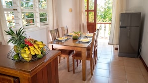 A dining area with a wooden table, chairs, and a fruit basket. There is a refrigerator to the right. - La Maison Hibiscus (Mahé Island)