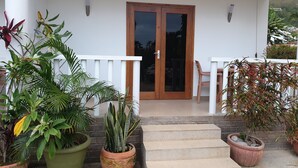 A covered porch with a wooden door, potted plants, and a white railing. - La Maison Hibiscus (Mahé Island)