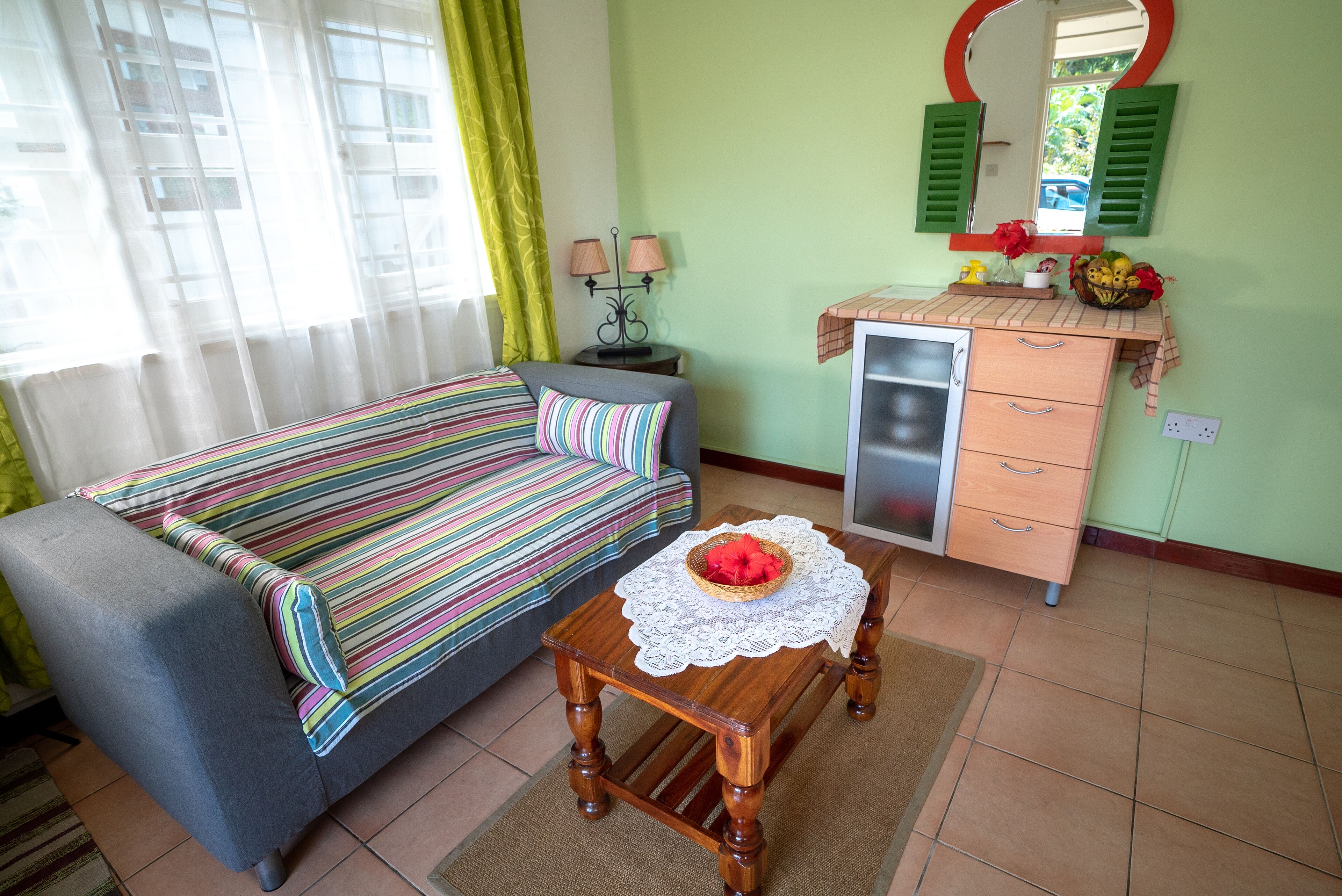 A room with a bed, a small table with a basket, a dresser, and a mirror.