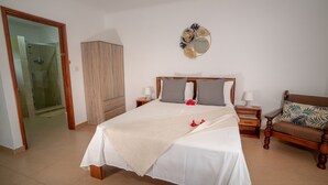 A bedroom with a bed, bedside tables, a wardrobe, a mirror, and a chair. - La Maison Hibiscus (Mahé Island)