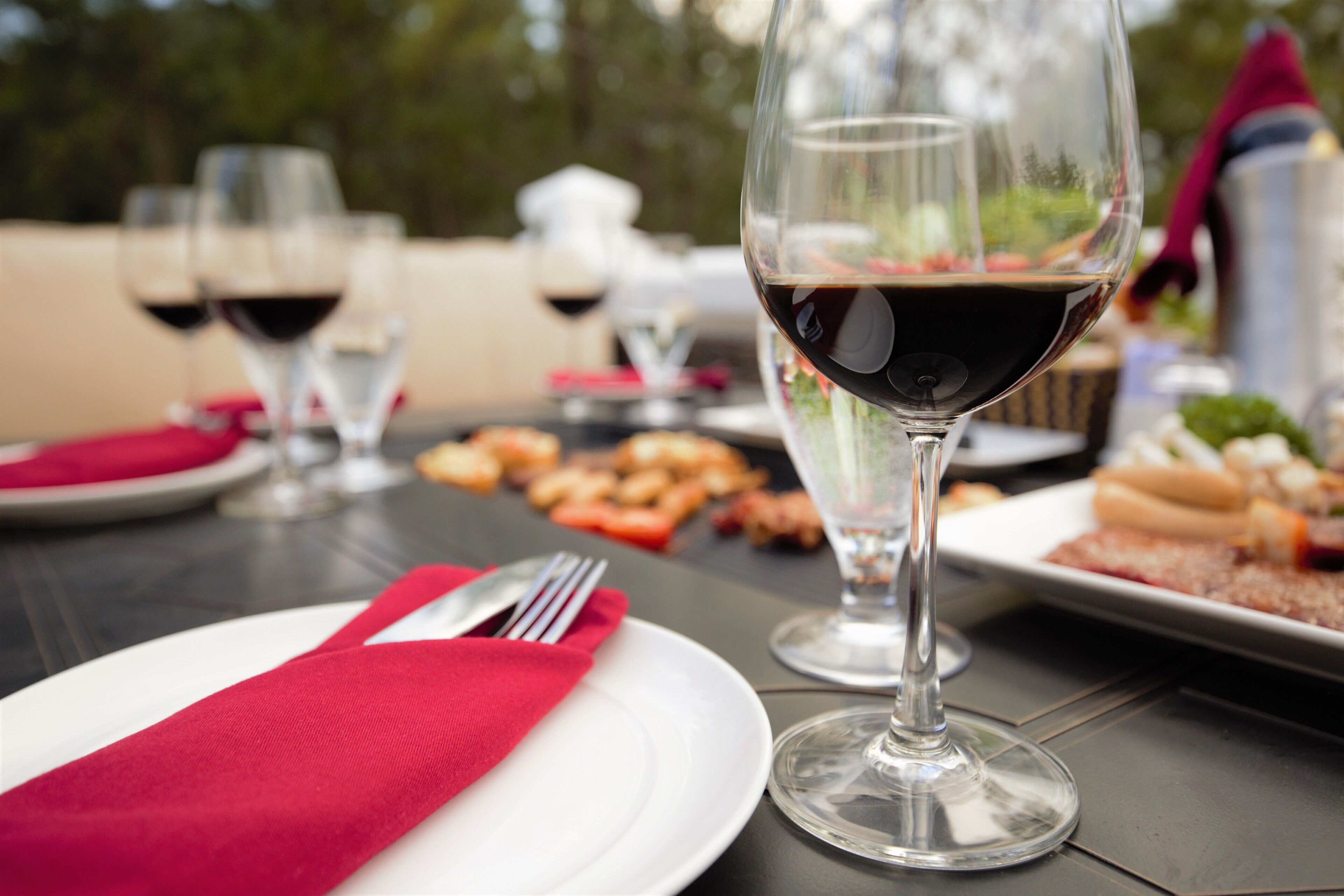 Una mesa de comedor con un mantelino rojo, una copa de vino y platos de comida.