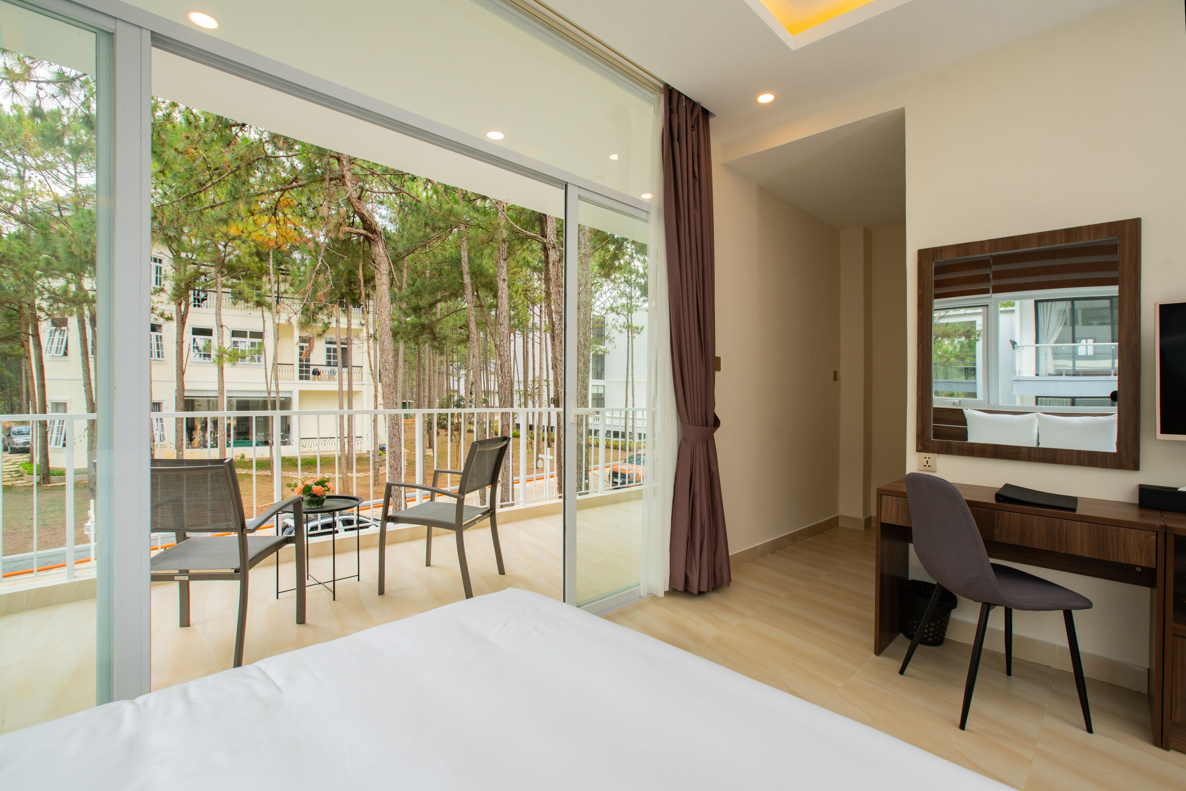 A hotel room with a large window, a bed, a desk, and a chair.