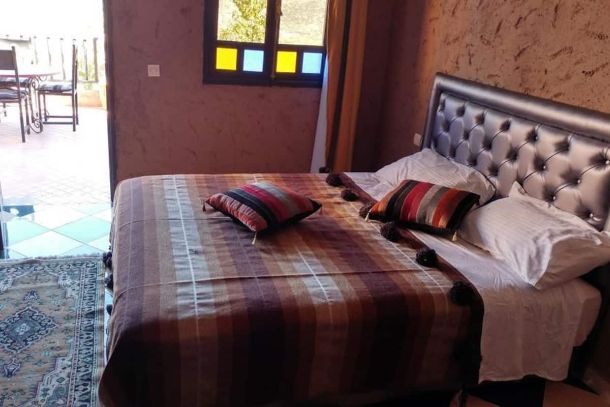 A bedroom with a bed, pillows, a window, and a view of an outdoor patio.