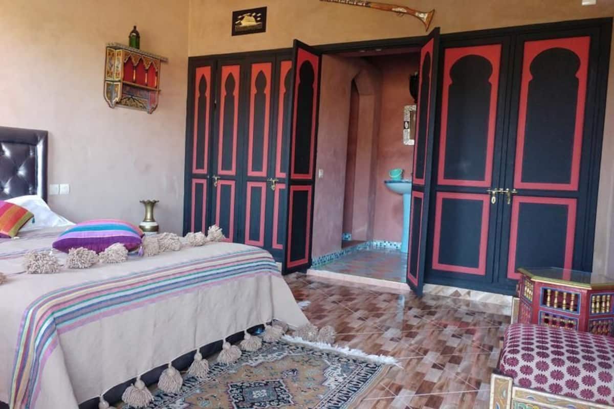 A bedroom with a large bed, a headboard, a bedside table, a nightstand, a window, and a door.