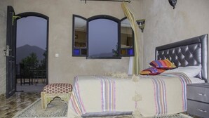 A bedroom with a bed, bedside table, and a window with curtains. - Dar Soulaimane Ourika (Ourika)