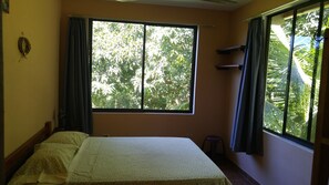 A room with a bed, a window with curtains, and a view of trees outside.