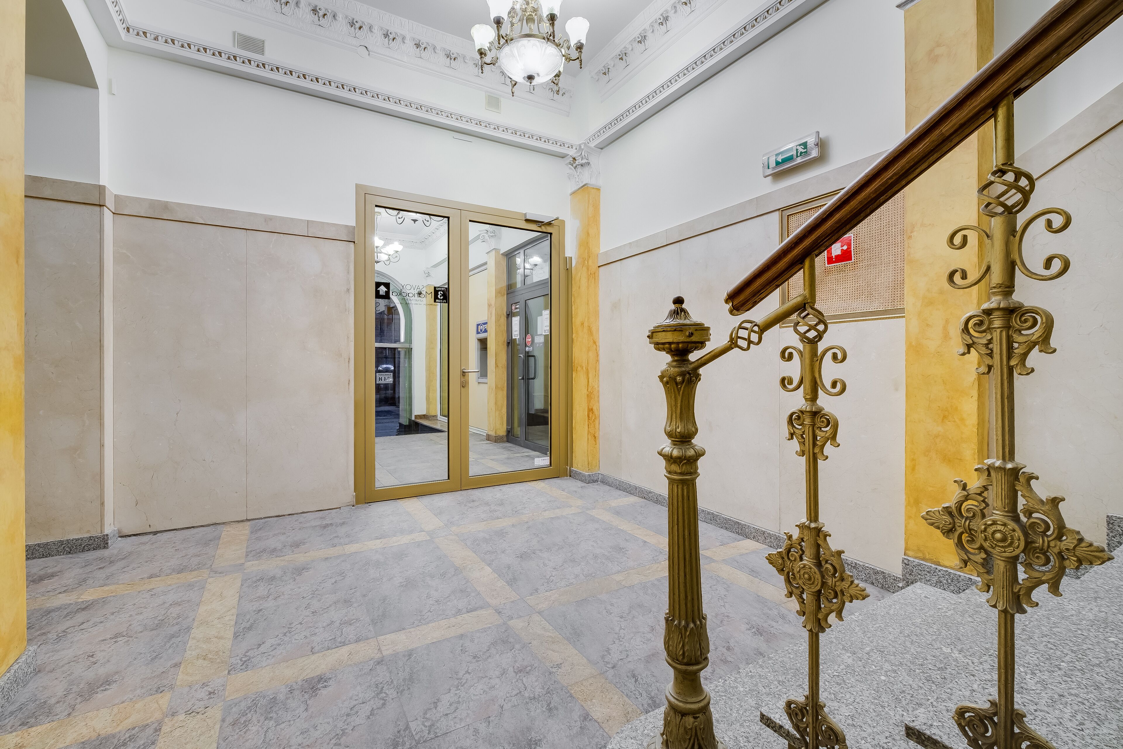 A spacious lobby with a marble floor, ornate golden railings, and a large mirror reflecting the interior.