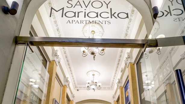 Imponente entrada a Savoy Mariačka Apartments, con una escalera central, techo ornamentado y un cartel sobre la entrada.
