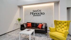 Una sala de estar moderna con un sofá de cuero negro, un sillón amarillo y una mesa de centro blanca. Un letrero en la pared dice "SAVOY Mariacka Apartments.".
