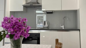 A modern kitchen with white cabinets, a stainless steel range hood, a built-in oven, and a coffee maker.