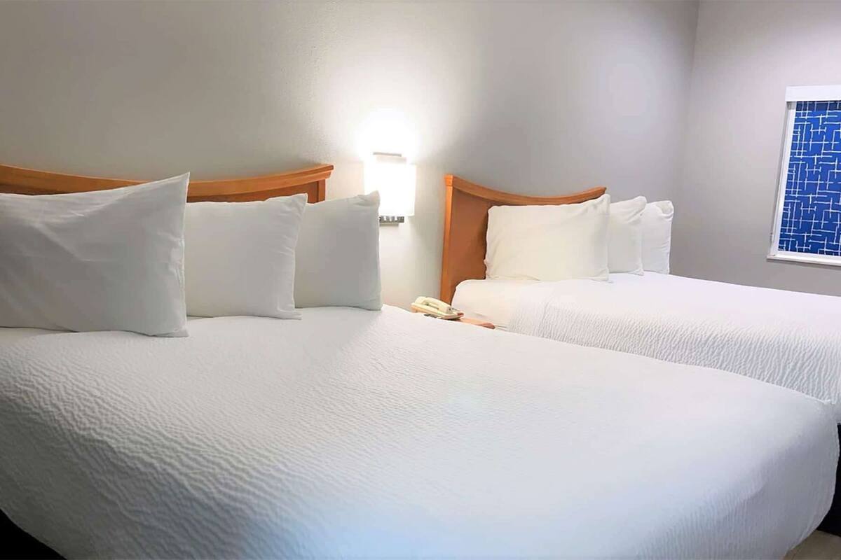 Two beds with white bedding, a wooden headboard, a bedside phone, and a window with a blue pattern.