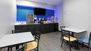 A bar area with a flat-screen TV, a coffee machine, and various snacks. There are four tables and chairs arranged for seating. - Days Inn by Wyndham North Little Rock/ Maumelle (North Little Rock)