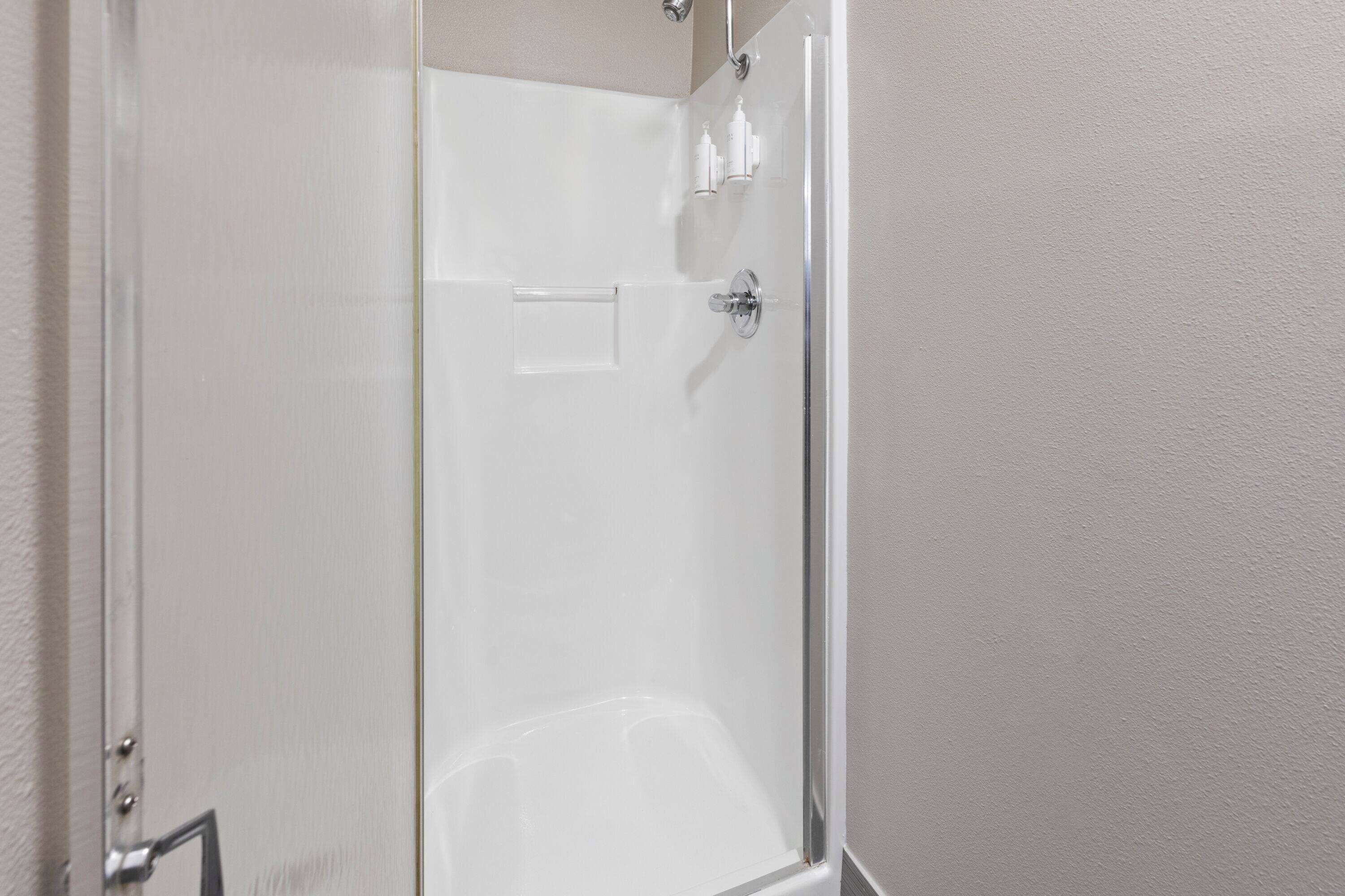 A clear glass shower enclosure with a chrome handle and a small shelf with toiletries.