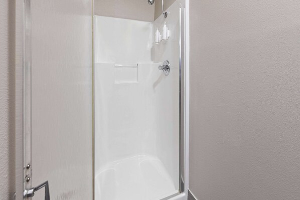 A clear glass shower enclosure with a chrome handle and a small shelf with toiletries.
