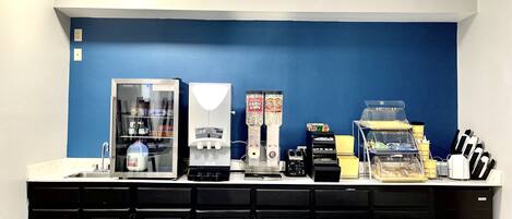 A kitchenette with a coffee machine, a milk dispenser, and a refrigerator.