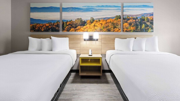A hotel room with two beds, a wooden headboard, a nightstand, and a large landscape painting above the beds. - Days Inn by Wyndham North Little Rock/ Maumelle (North Little Rock)