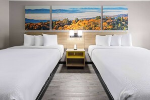 A hotel room with two beds, a wooden headboard, a nightstand, and a large landscape painting above the beds.