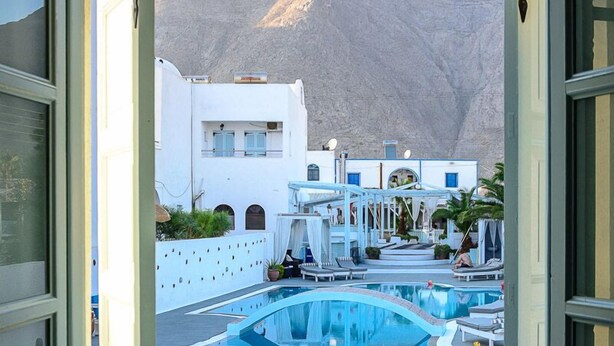 A view from a window of a pool area with a mountain in the background. - Aeolis Santorini (Santorini)