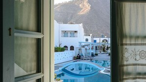 A view from a room with a door open, overlooking a pool area with white buildings and a mountain in the background. - Aeolis Santorini (Santorini)
