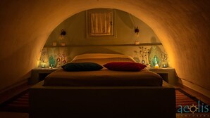 A cozy, arched room with a bed, two bedside tables, and a window with curtains. - Aeolis Santorini (Santorini)