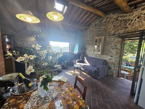 A rustic interior with a stone wall, a wooden ceiling, a dining table with a floral tablecloth, and a sofa.