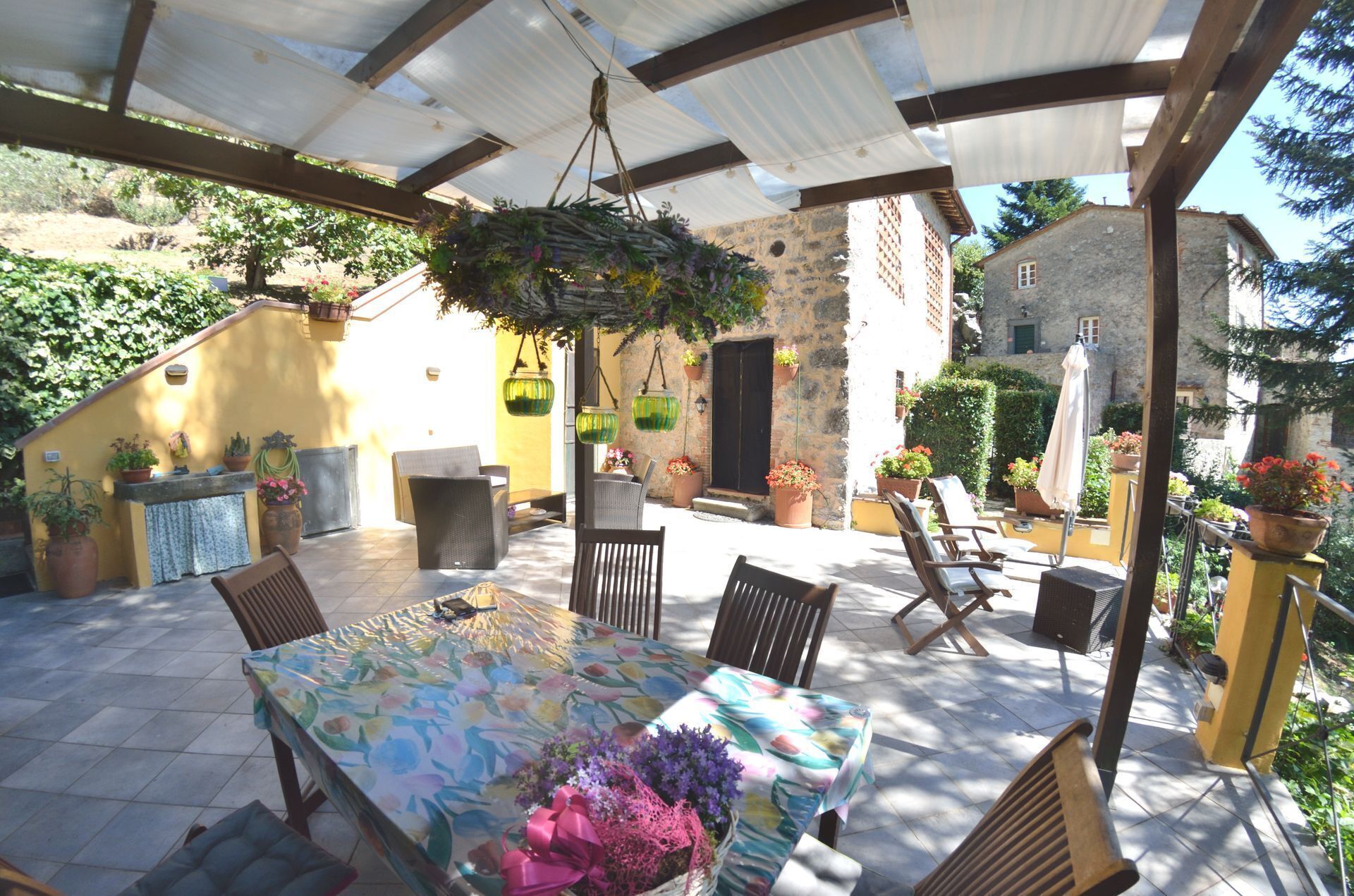 Une terrasse extérieure avec une table dressée pour le repas, entourée de chaises et agrémentée de différentes plantes en pot.