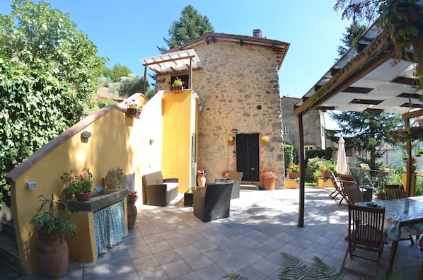 A courtyard with a stone building, outdoor seating, and potted plants.