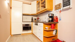 Una cocina con armarios blancos, encimera de madera, una cafetera y una cesta con cojín rojo.