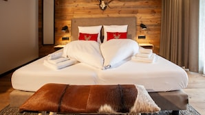 A bedroom with a wooden ceiling, a bed with white bedding and red pillows, a mounted deer skull, and a brown leather ottoman. - 1102 Kristall 2 (Gaschurn)